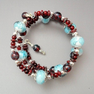 May include: A multi-strand bracelet with red and blue glass beads. The beads are round and have a mottled appearance. The bracelet has a silver clasp.