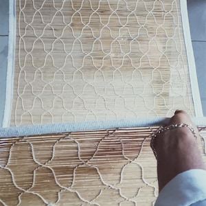 May include: A rectangular bamboo mat featuring a light tan natural finish with a white woven lattice pattern overlay. The mat is framed with a white fabric border and displays a grid of thin vertical bamboo reeds held together by white thread.