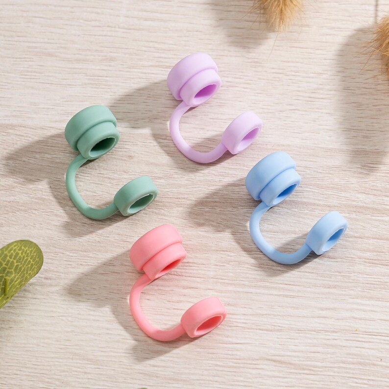 May include: Four colorful silicone bottle stoppers in pastel shades of green, purple, pink, and blue. Each stopper has a curved design with a circular top and a smaller circular end.