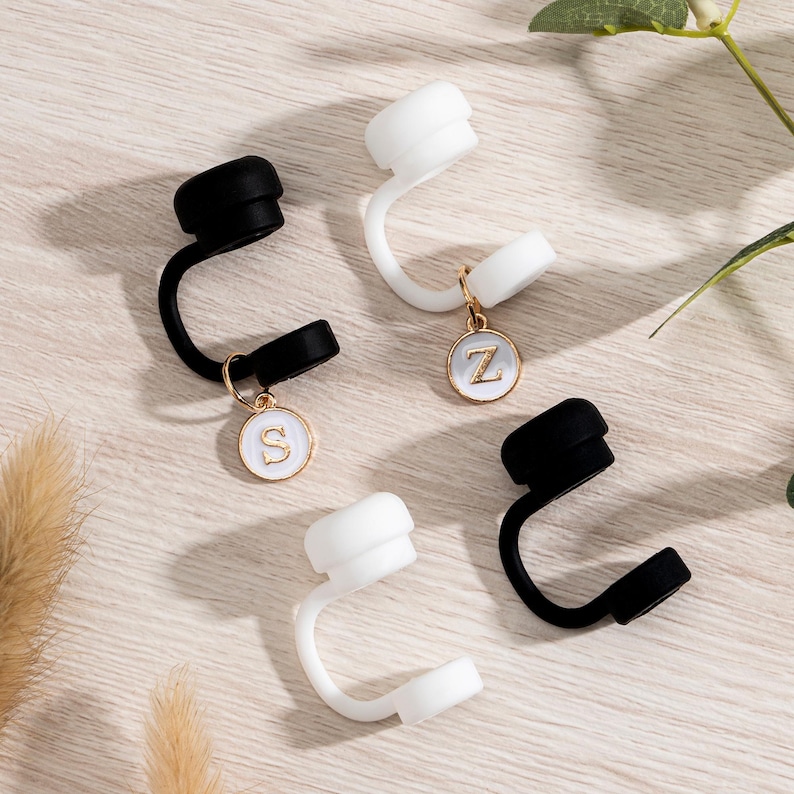 May include: Four bottle stoppers, two black and two white, with a curved design. Each stopper has a small, round charm with a gold border and a white center, displaying the letters "S" and "Z".