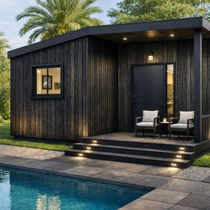 May include: A modern, dark-stained wooden cabin with a flat roof, a small porch, and a pool. The cabin has a black door, windows, and two chairs on the porch. The steps are illuminated with lights, and the setting is surrounded by greenery.