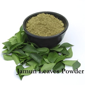 May include: A black bowl filled with green powder, surrounded by fresh green leaves. The text "Jamun Leaves Powder" is displayed at the bottom of the image. The powder and leaves are on a white background.