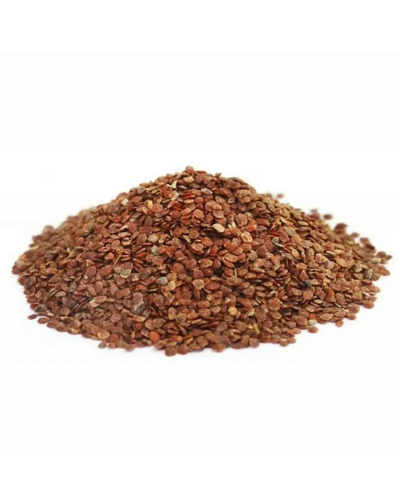 May include: A pile of small, reddish-brown seeds against a white background. The seeds are oval-shaped and appear to be dried. The image is a close-up, showing the texture and color variations within the seed pile.