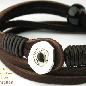 May include: A brown leather bracelet with a silver, geometric charm. The bracelet is 21cm long.
