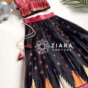 Puede incluir: Un conjunto de dos piezas con un top estampado en rosa y dorado y una falda negra con detalles dorados, naranjas y blancos. La falda tiene un borde decorativo y el texto "ZIARA COUTURE".