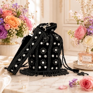 Könnte beinhalten: Eine schwarze Samt-Beuteltasche mit aufwendigen Perlenstickereien und klaren Kristallakzenten in Blumenmustern. Die Tasche verfügt über einen passenden Perlen-Schulterriemen, einen Kordelzugverschluss und einen dekorativen Perlenfransenbesatz.