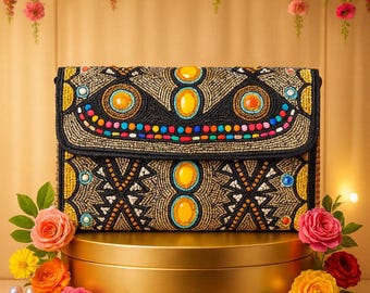 May include: A black beaded clutch with a geometric pattern and large yellow and blue accents. The clutch is displayed on a gold pedestal, surrounded by colorful flowers and pearls. The background features a floral arrangement.