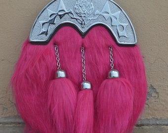 May include: A hot pink sporran with a silver cantle featuring a thistle design. The sporran has three matching pink tassels hanging from the bottom and silver chain details.