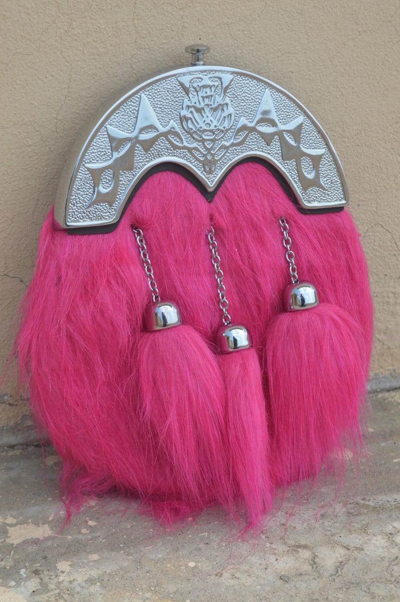 Puede incluir: Un sporran rosa intenso con un cantle plateado. El sporran tiene una textura esponjosa y tres borlas con tapa plateada colgando de cadenas. El cantle est&aacute; decorado con dise&ntilde;os en relieve.