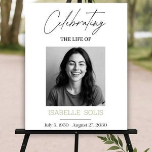 Könnte beinhalten: Ein Gedenkschild auf einer schwarzen Staffelei. Auf dem Schild steht "Celebrating The Life Of" über einem Schwarz-Weiß-Foto einer lächelnden Frau. Unter dem Foto stehen der Name "ISABELLE SOLIS" und die Daten "5. Juli 1950 - 27. August 2030".