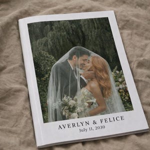 Könnte beinhalten: Ein weißes Hochzeitsfotoalbum mit einem romantischen Bild eines Paares, das sich unter einem Schleier küsst. Das Albumcover zeigt die Namen "AVERLYN & FELICE" und das Datum "July 11, 2030" in einer einfachen Schriftart. Der Hintergrund ist neutral.