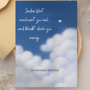 May include: A greeting card with a blue sky background and white cloud illustrations. The card features the German text "Jedes Wort erscheint zu viel und bleibt doch zu wenig" and "IN GEDANKEN BEI EUCH". A small white heart is also visible.