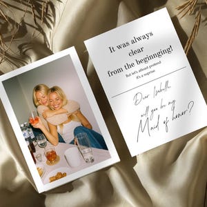 Könnte beinhalten: Zwei weiße Karten mit schwarzem Text. Eine Karte zeigt ein Foto von zwei Frauen, die sich umarmen und trinken. Die andere Karte lautet "It was always clear from the beginning!" und "Dear Isabelle, will you be my Maid of honor?"