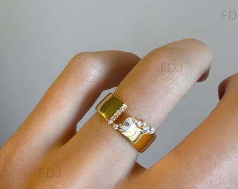 May include: A gold-toned open-style ring featuring a wide, polished band with a gap. One side of the opening is accented with a row of small, clear, round stones, while the other side features a cluster of clear, pear-shaped and round stones.