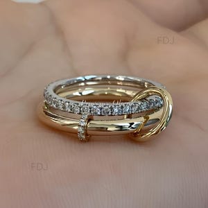 May include: A multi-band ring featuring a silver-toned band encrusted with small clear stones and a smooth, polished gold-toned band that loops through the silver band. A small vertical connector piece set with clear stones joins the two bands.