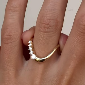 May include: A curved yellow gold band ring featuring five round brilliant cut diamonds set along one side of the arch. The polished metal band has a smooth, tapered design that follows the contour of the finger, showcasing clear stones.
