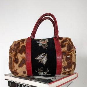 May include: A red and black leopard print handbag with embroidered floral details. The bag has two red leather handles and a zipper closure.