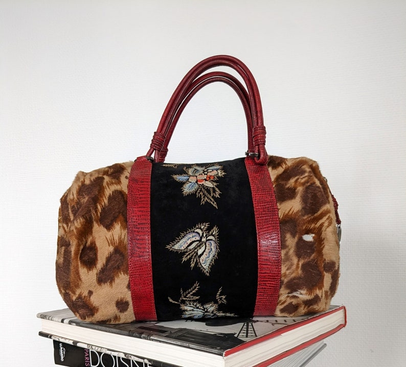 May include: A red and black leopard print handbag with embroidered floral details. The bag has two red leather handles and a zipper closure.