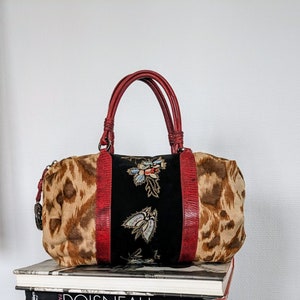 May include: A red, brown, and black leopard print handbag with a black velvet panel featuring embroidered floral designs. The bag has a top handle and a zipper closure.