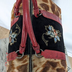 May include: A brown and black animal print handbag with red leather handles and a black suede panel with embroidered flowers. The bag has a zipper closure.