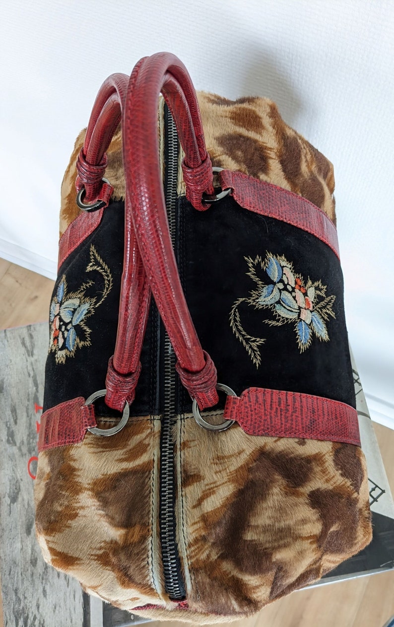 May include: A brown and black animal print handbag with red leather handles and a black suede panel with embroidered flowers. The bag has a zipper closure.