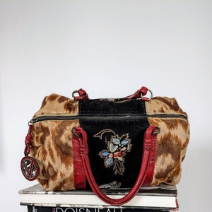May include: A brown and black patchwork handbag with red leather straps and a floral embroidered design. The bag has a zipper closure and a metal charm.