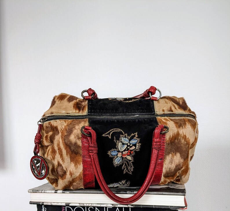 May include: A brown and black patchwork handbag with red leather straps and a floral embroidered design. The bag has a zipper closure and a metal charm.
