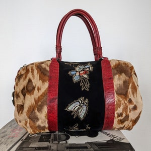 May include: A brown and tan leopard print handbag with red leather handles and trim. The bag has a black velvet panel with embroidered flowers in gold, blue, and red.