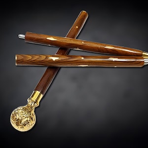 Könnte beinhalten: Gehstock aus dunklem, braunem Holz, akzentuiert mit goldfarbenen Metalldetails. Der Griff ist eine dekorative goldene Kugel. Der Stock ist mit eingelegten goldfarbenen Akzenten am Schaft versehen.