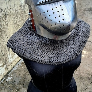 Op de afbeelding: Een middeleeuwse helm van glanzend metaal met een puntige bovenkant en een vizier met kleine gaatjes. Wordt geleverd met een mali&euml;nkolder kraag, gepresenteerd op een zwarte mannequin. Ideaal voor re-enactment.