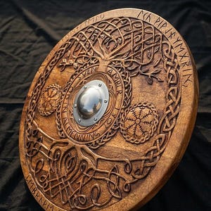 Op de afbeelding: Een ronde houten schild met ingewikkelde gravures. Het schild heeft een centrale metalen baas, een levensboomontwerp en runeninscripties. Het hout heeft een warme, bruine tint en de gravures zijn gedetailleerd en gestructureerd.