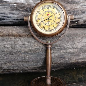 Puede incluir: Reloj de escritorio antiguo de color latón con números romanos en la esfera. El reloj tiene un soporte y una base decorativa. La esfera del reloj tiene las palabras "White Star Line" y "Titanic".