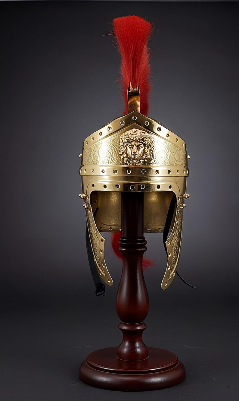 May include: A gold-colored Roman helmet with a red plume, displayed on a wooden stand. The helmet features a detailed face design and decorative rivets. The helmet is a historical replica.