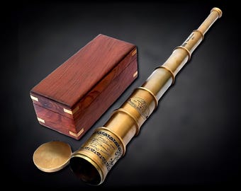 May include: A brass telescope with a wooden box. The telescope is extended and has engraved details. The wooden box is rectangular with brass corner accents. The telescope's cap is also brass. The items are on a black background.