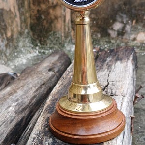 Può includere: Telegrafo di comando motore navale in ottone e legno. Il quadrante mostra comandi di velocità come "Lento" e "Tutto" in nero e rosso. La base è in legno scuro e lo stelo è in ottone.