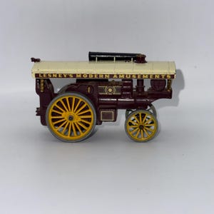 May include: A vintage toy steam engine in maroon and cream with yellow wheels. The toy has the text "LESNEY'S MODERN AMUSEMENTS" printed on the side. The steam engine has a black smokestack and is a collectible toy.