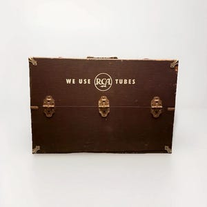 May include: A vintage brown wooden box with metal hardware and corner protectors. The box has the text "WE USE RCA TUBES" in white lettering. The box has three metal latches and a handle.