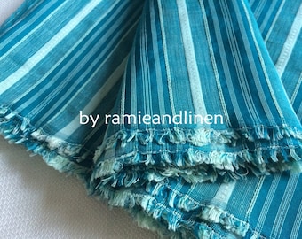 May include: Teal and white striped fabric with a frayed edge. The fabric is folded in layers and the text "by ramieandlinen" is visible.