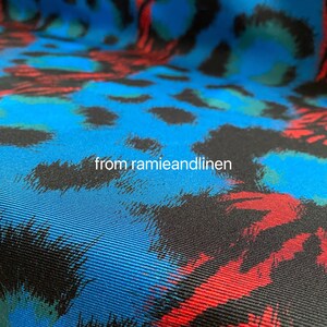 May include: Close-up of a blue fabric with a black, red, and green animal print. The fabric has a textured, woven appearance.