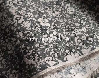 May include: Close-up of a gray fabric with a white floral pattern. The fabric has a subtle texture and a slightly frayed edge. "from ramieandlinen" is printed on the fabric.