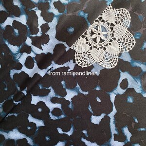 May include: Black fabric with a blue and white abstract print. A white crocheted doily is on top of the fabric. The text "from ramieandlinen" is visible in the lower center of the image.