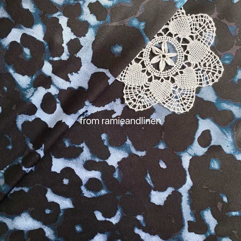 May include: Black fabric with a blue and white abstract print. A white crocheted doily is on top of the fabric. The text "from ramieandlinen" is visible in the lower center of the image.