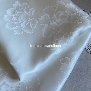 May include: White fabric with an embossed floral pattern. The fabric is folded in half and the text "from ramieandlinen" is visible.