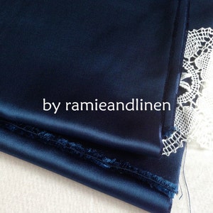May include: A close-up of a deep blue satin fabric with a folded edge. The fabric is folded over itself and the edge is visible. The fabric is smooth and silky. The fabric is next to a white lace fabric.