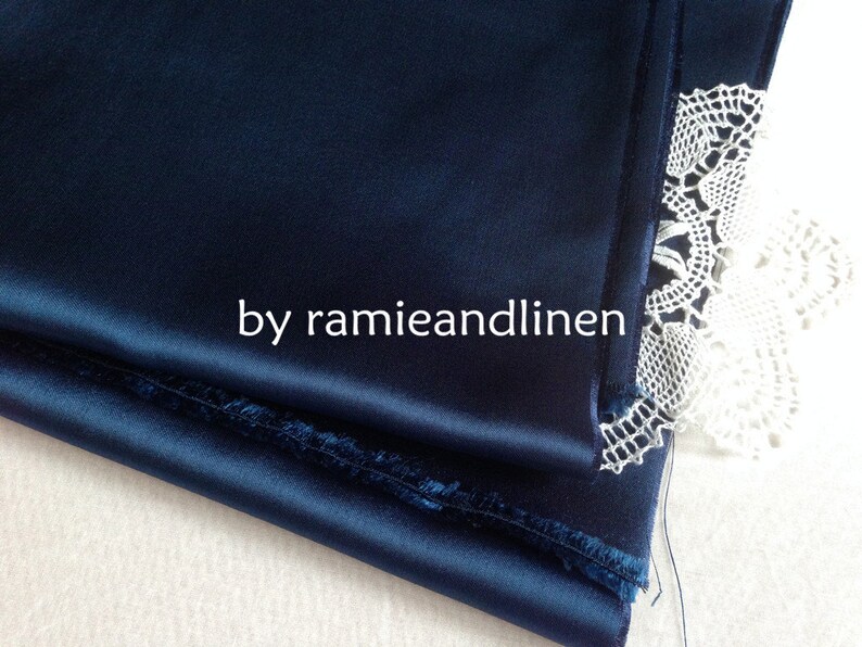 May include: A close-up of a deep blue satin fabric with a folded edge. The fabric is folded over itself and the edge is visible. The fabric is smooth and silky. The fabric is next to a white lace fabric.