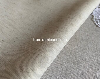 Puede incluir: Primer plano de una tela beige claro con un brillo sutil. La tela está doblada por la mitad y el pliegue es visible en el centro de la imagen. El texto "from ramieandlinen" es visible en la parte inferior central de la imagen.