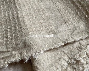 Pode incluir: Um close-up de um tecido de linho bege com textura de waffle e bordas desfiadas. O tecido é texturizado e tem um visual natural e rústico. O texto "from ramieandlinen" é visível na parte inferior central da imagem.