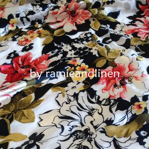 May include: White fabric with a black background and a large floral print in shades of red, pink, white, and yellow. The fabric has a satin-like sheen. The text "by ramieandlinen" is printed on the fabric.