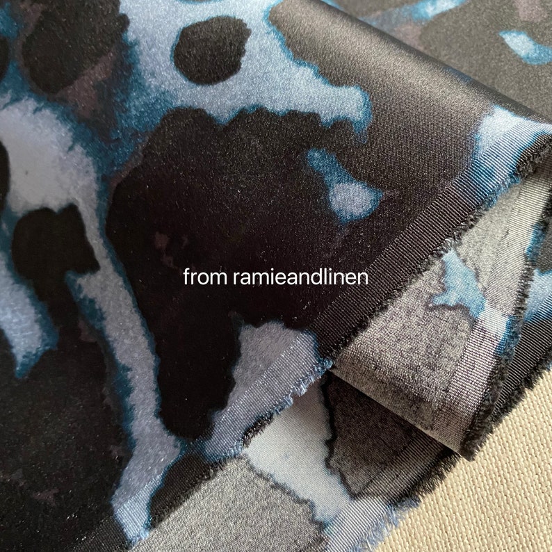 May include: Close-up of a black and blue fabric with a mottled pattern. The fabric has a smooth, silky texture and is folded over on itself. The text "from ramieandlinen" is visible in the lower left corner of the image.