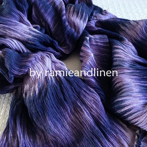 Puede incluir: Una bufanda de rayas moradas y azules con textura arrugada. La bufanda est&aacute; doblada por la mitad y el texto "by hamieandlinen" es visible en el centro.